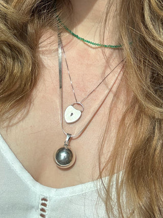 Sterling silver chime ball pendant worn on a long chain among layered necklaces.