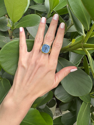 Blue chalcedony intaglio ring worn on a hand.