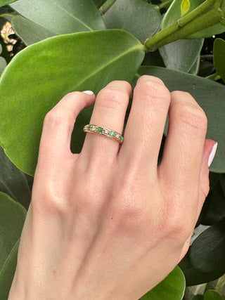 Vintage gold emerald and diamond band worn on a hand against green leaves.