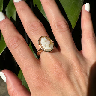 Vintage gold oval shell cameo ring worn on a hand, showing its carved portrait and bezel frame.