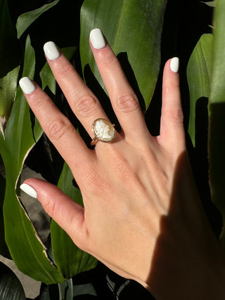 Vintage gold oval shell cameo ring worn on a hand, showing its carved portrait and bezel frame.