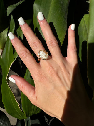 Vintage gold oval shell cameo ring worn on a hand, showing its carved portrait and bezel frame.