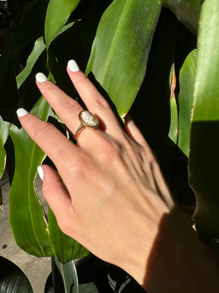Vintage gold oval shell cameo ring worn on a hand, showing its carved portrait and bezel frame.