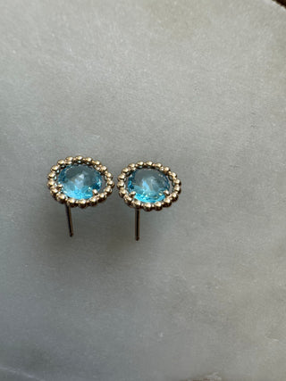 Angled view of blue topaz stud earrings showing their gold frames and projecting posts.