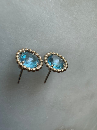 Angled view of blue topaz stud earrings showing their gold frames and projecting posts.