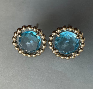 Close-up of the faceted blue topaz stones and rounded gold frames in stud earrings.