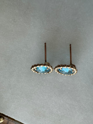 Side view of blue topaz stud earrings showing their gold settings and posts.