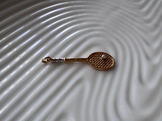 Gold tennis racket pendant with contrasting handle details and a small ball.
