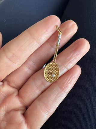 Gold tennis racket pendant held in a palm to show its size.