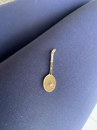 Back view of a gold tennis racket pendant on navy fabric.