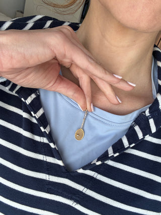 Gold tennis racket pendant worn on a chain over a blue top.