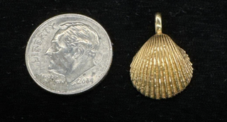 Gold seashell pendant beside a dime for size comparison.